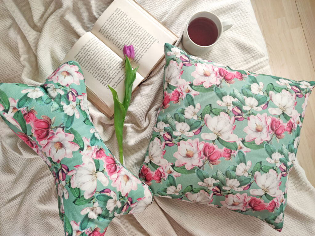 Leseknochen und Kissen mit Magnolienblüten auf Decke – gemütlicher Lese-Moment